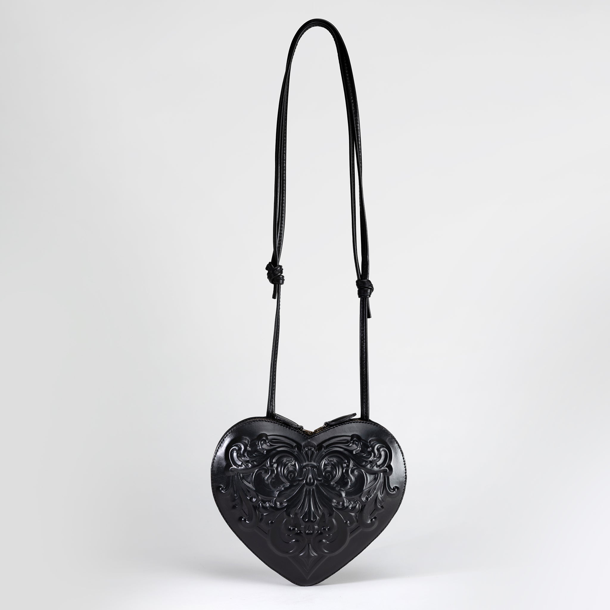 Flatlay of handmade heart-shaped leather bag in black, sculpted in Renaissance baroque style. Pictured with soft shadows to show texture and relief.